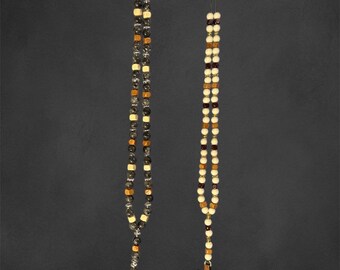 May include: Two rosaries with wooden cross pendants. One rosary features a mix of black, tan, and white beads, while the other has cream and brown beads. Both hang against a dark gray background.