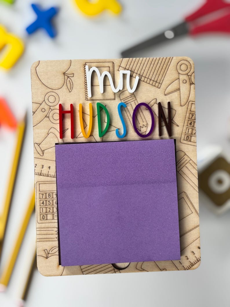 Pu&ograve; includere: Organizzatore da scrivania per insegnanti in legno con il nome "HUDSON" in lettere colorate e "mr" in bianco. L'organizzatore ha un blocco note viola ed &egrave; decorato con illustrazioni a tema scolastico, tra cui matite, forbici e mele.