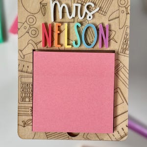 Pu&ograve; includere: Lavagna memo in legno con il nome "Mrs. Nelson" a lettere colorate. Include un blocco note rosa e disegni a tema scolastico incisi, come forbici e matite. Un regalo premuroso per un insegnante.