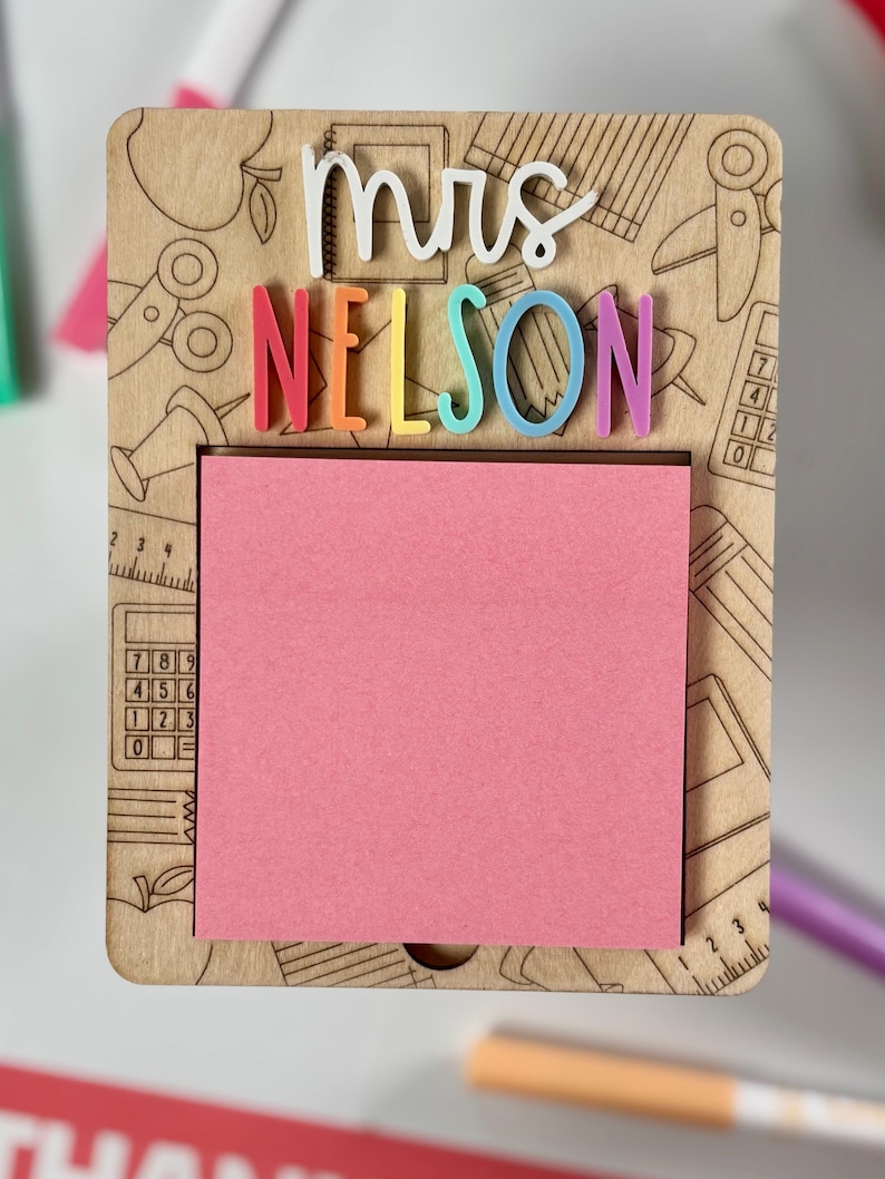 Pu&ograve; includere: Lavagna memo in legno con il nome "Mrs. Nelson" a lettere colorate. Include un blocco note rosa e disegni a tema scolastico incisi, come forbici e matite. Un regalo premuroso per un insegnante.
