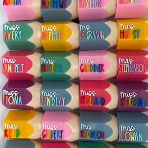 May include: A collection of pencil-shaped containers in various colors, each featuring a raised white title such as Mrs, Miss, or Ms, followed by a name in colorful, individual letters. The containers have a beige tip and a hexagonal body.