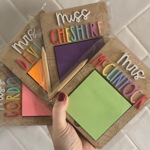 Pu&ograve; includere: Una collezione di regali personalizzati per insegnanti, ognuno con un blocco note con un post-it colorato, una matita e un nome in lettere vivaci. I nomi includono "Mrs. Gordon", "Mrs. Devi", "Mrs. Cheshire" e "Mrs. McClintock".