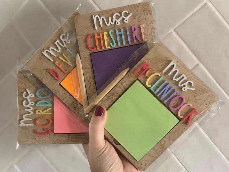 Pu&ograve; includere: Una collezione di regali personalizzati per insegnanti, ognuno con un blocco note con un post-it colorato, una matita e un nome in lettere vivaci. I nomi includono "Mrs. Gordon", "Mrs. Devi", "Mrs. Cheshire" e "Mrs. McClintock".