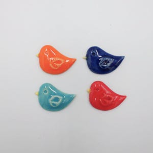 Könnte beinhalten: Vier bunte Keramikvögel in Orange, Marineblau, Türkis und Rot. Jeder Vogel hat einen kleinen gelben Schnabel und ein weißes Design. Die Figuren sind auf weißem Hintergrund angeordnet. Jede Figur ist etwa 5 cm groß.