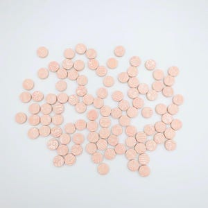 May include: A collection of small, light peach-colored, round wooden discs scattered on a white surface. Each disc has a textured, patterned design on its surface, creating a visually interesting arrangement. The discs are evenly spaced.