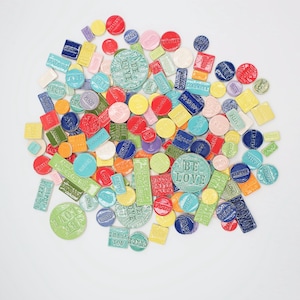May include: A selection of brightly coloured ceramic tiles in various shapes, including circles, squares, and rectangles. The tiles are in shades of red, blue, green, yellow, and pink. Some tiles have embossed words like "BE LOVE", "THANK YOU", and "GRACE".