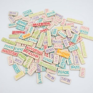 May include: A collection of rectangular tiles with positive words like "Gratitude", "Peace", and "Hope" in various colors. The tiles are scattered on a white surface, creating a visually appealing arrangement.