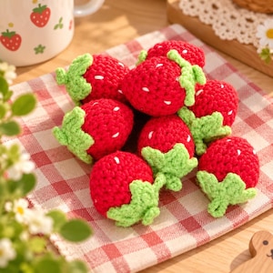 May include: A collection of small, handmade crocheted strawberries featuring bright red yarn bodies with textured surfaces, green yarn leaves at the top, and small white yarn stitches scattered across the exterior to represent seeds.