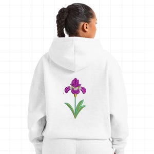 May include: A white hoodie with a purple iris flower design on the back. The flower has purple petals with white accents, green leaves, and a green stem. The hoodie is made of a soft, comfortable material.