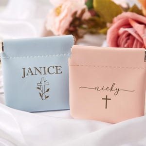 May include: Two small, personalized pouches with a cross design. One pouch is light blue with the name "JANICE" and the other is pink with the name "nicky".