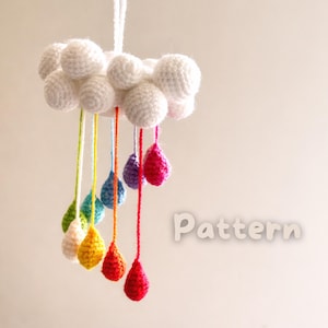 May include: A handmade crochet cloud mobile with white cloud shapes and colorful raindrop pendants. The raindrops are in shades of green, yellow, orange, blue, purple, and red. The word "Pattern" is visible in the image.