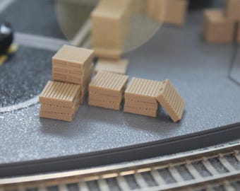 May include: A set of five miniature wooden pallets, stacked and arranged on a gray surface. The pallets are made of light brown wood and have a realistic appearance.