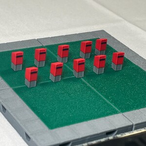 May include: A set of 10 miniature red post boxes on a green and grey surface. The post boxes are arranged in two rows of five.