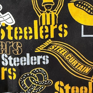 Könnte beinhalten: Schwarzer Stoff mit gelben und weißen Grafiken des Pittsburgh Steelers Footballteams. Enthält das Teamlogo, Helm, Football, Torpfosten und die Wörter "Steelers" und "Steel Curtain".