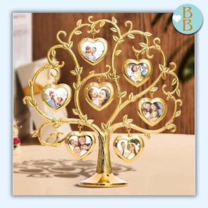 Può includere: Un albero portafoto in metallo color oro con cornici a forma di cuore. L'albero ha un tronco, rami e foglie, con sette cornici a forma di cuore appese ai rami, ognuna contenente una fotografia. L'albero poggia su una base rotonda.