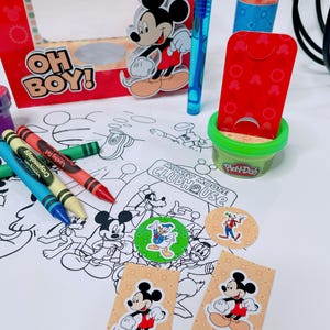 May include: A colorful Mickey Mouse Clubhouse-themed party set. Includes a red box with Mickey, crayons, Play-Doh, stickers, and a coloring sheet. The box reads "OH BOY!" and "CLUBHOUSE".