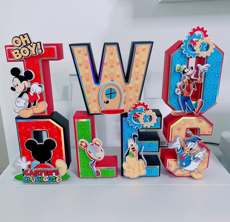 K&ouml;nnte beinhalten: Eine farbenfrohe, dreidimensionale Anzeige mit den Buchstaben "TWO" und "DOLLS" mit Disney-Charakter-Ausschnitten. Die Buchstaben sind rot, blau, gr&uuml;n und gelb, mit Micky Maus, Goofy, Pluto und Donald Duck. Der Text "OH BOY!" und "CARTER'S CLUBHOUSE" ist enthalten.