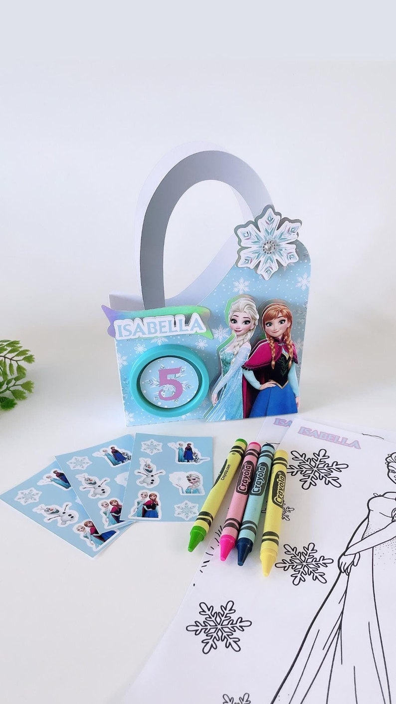 May include: A Frozen-themed party favor bag with a blue and white snowflake design. The bag has a handle and is decorated with images of Elsa and Anna. The bag also includes a sticker sheet with images of Elsa, Anna, and Olaf, four crayons, and a coloring page featuring Elsa.