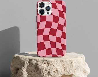 Puede incluir: Una funda de teléfono a cuadros rosa y roja con un patrón ondulado. La funda está sobre una roca de color claro.