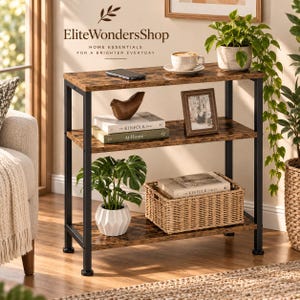 May include: A three-tier console table with a dark brown wood-grain finish and a black metal frame. The shelves hold a smartphone, a ceramic mug, a wooden bird figurine, two books titled The Kinfolk Home, a picture frame, and a potted plant.