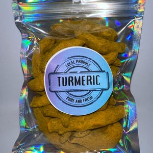 May include: A clear plastic bag with a resealable zipper closure contains dried turmeric root pieces. The bag has a holographic iridescent finish. A round sticker on the bag reads "Local Product Turmeric Pure and Fresh".