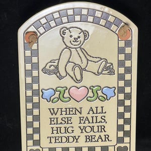 May include: A ceramic wall plaque with a chequered border and a teddy bear illustration. The plaque has the text "When all else fails, hug your teddy bear."