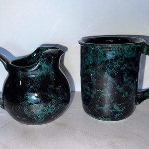 May include: A green and black ceramic pitcher and mug with a marbled glaze.