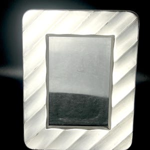 May include: A rectangular silver picture frame with a textured, diagonal stripe design. The frame has rounded corners and a simple, elegant aesthetic. The frame holds a black and white image.
