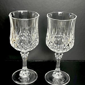 May include: Two clear crystal wine glasses with diamond-cut patterns on the bowl and stem. The glasses have a tulip shape and sit on a round base. The background is black.