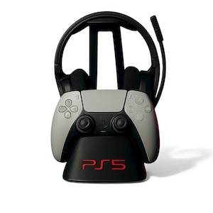 Peut inclure: Un support de casque noir avec une manette de jeu grise et blanche et un casque noir. La base du support porte le texte rouge "PS5". La manette a la disposition standard des boutons.