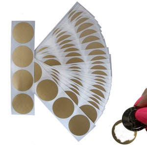 May include: A sheet of 25 gold round stickers, each about the size of a US quarter. The stickers are arranged in a fan shape, with the top sticker partially visible. The stickers are on a white background.