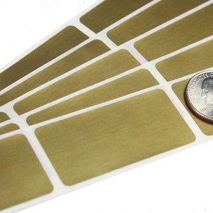 May include: A stack of gold-colored rectangular labels with white borders. The labels are approximately the size of a US quarter.