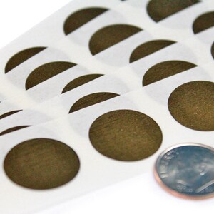 May include: A sheet of brown circle stickers with a wood grain texture. The stickers are arranged in rows and are about the size of a US dime.