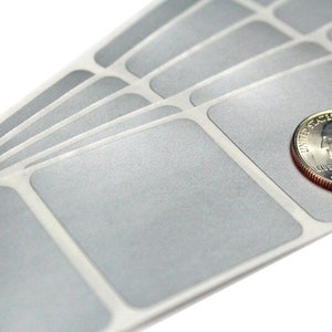 May include: A sheet of silver, adhesive labels with rounded corners. The labels are arranged in rows and columns. A US quarter is placed on top of the labels to show the size.
