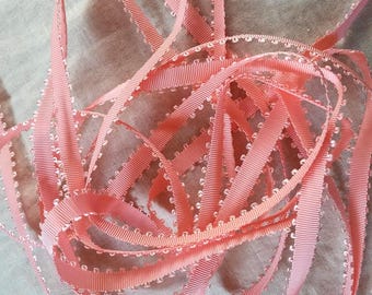 May include: A close-up of a pink ribbon with a scalloped edge. The ribbon is made of a soft, silky material and has a delicate, feminine look.