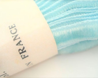 May include: A roll of light blue, textured, fabric ribbon with a white label that reads "Made in France" and "83".