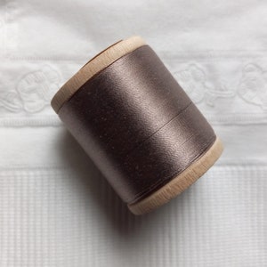 Könnte beinhalten: Eine Spule mit metallischem braunem Garn, das um eine Holzspule gewickelt ist.