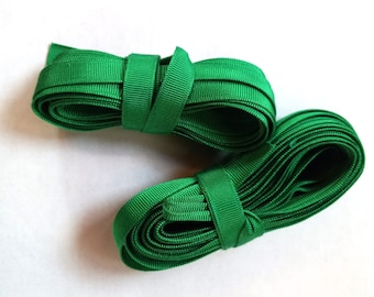 May include: Two spools of bright green grosgrain ribbon are displayed against a white background. Each spool is neatly coiled and secured with a matching ribbon band. The ribbon has a textured, ribbed appearance.