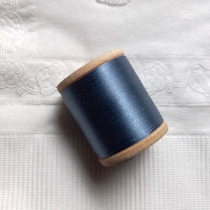 May include: A spool of dark blue thread wound around a wooden bobbin.
