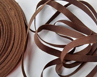 May include: A roll of brown woven ribbon, with a loose end of the ribbon lying next to it.