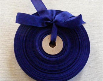May include: A spool of deep blue ribbon with a bow tied at the top. The ribbon is wound around a cardboard spool with a hole in the center.