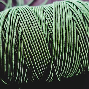 May include: Close-up of a tightly wound ball of green yarn. The yarn is composed of numerous parallel strands, creating a textured surface. The color is a muted, earthy green, suggesting a natural fiber. Ideal for knitting or crochet projects.