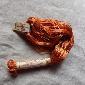 May include: A spool of orange Mallard Floss embroidery thread with a label that reads "Pursalls Mallard Floss (Registered Trade Mark) Boiling Dyes Made in Great Britain."