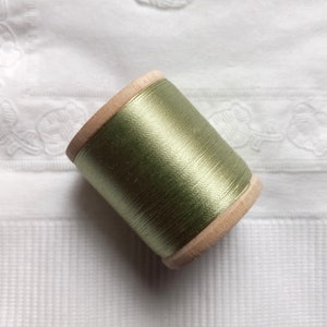 May include: A spool of green thread wound around a wooden bobbin.