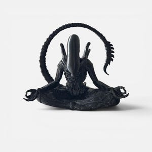 May include: A black sculpture of an Alien creature in a seated yoga pose. The creature has a long, curved tail and is in a meditative position with its hands in a mudra. The sculpture is set against a white background.