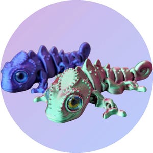 May include: Two 3D printed chameleon figurines, one blue and one green with red accents. The figurines have large eyes and detailed scales.