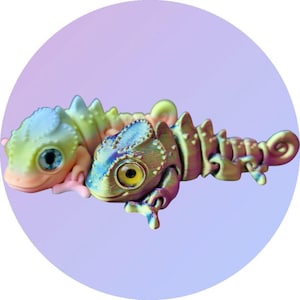 May include: Two chameleon figurines, one is green and blue with iridescent detailing, the other is a light green and pink with a blue eye.