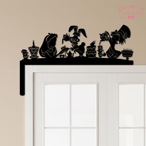 Pode incluir: Silhueta preta de uma cena de chá de Alice no País das Maravilhas. O design apresenta Alice, o Chapeleiro Maluco, a Lebre de Março e várias xícaras de chá, bules e bolos. O design é montado em uma prateleira preta.