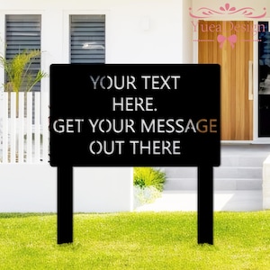 May include: Black metal yard sign with the text "YOUR TEXT HERE. GET YOUR MESSAGE OUT THERE." The sign has a rectangular shape with two supporting posts. The sign is placed on a green lawn in front of a white house.