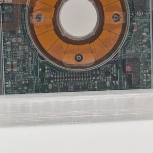 May include: A close-up of a circuit board with a circular, orange component in the center. The circuit board is mounted on a clear, plastic base.